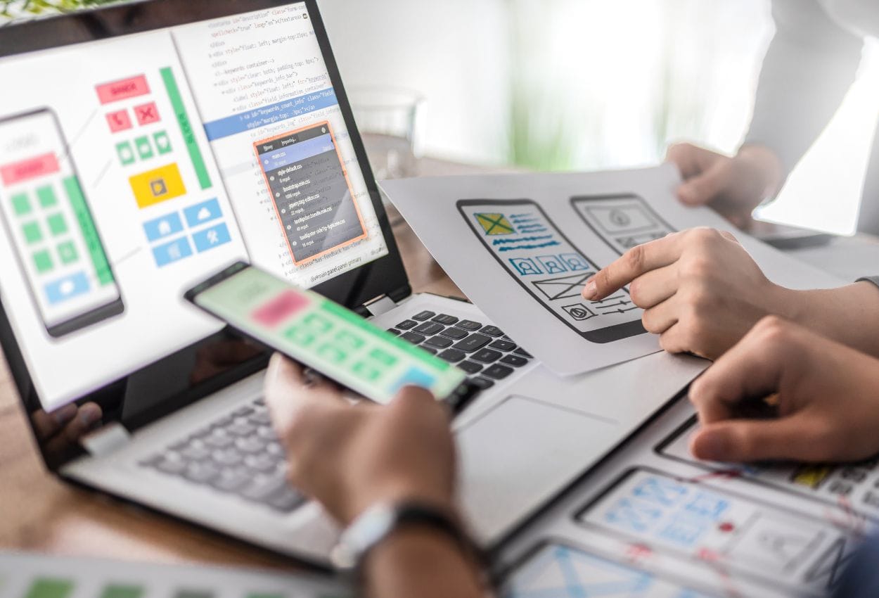 Equipo diseñando interfaz UX/UI en computadora y dispositivos móviles durante proceso de diseño web
